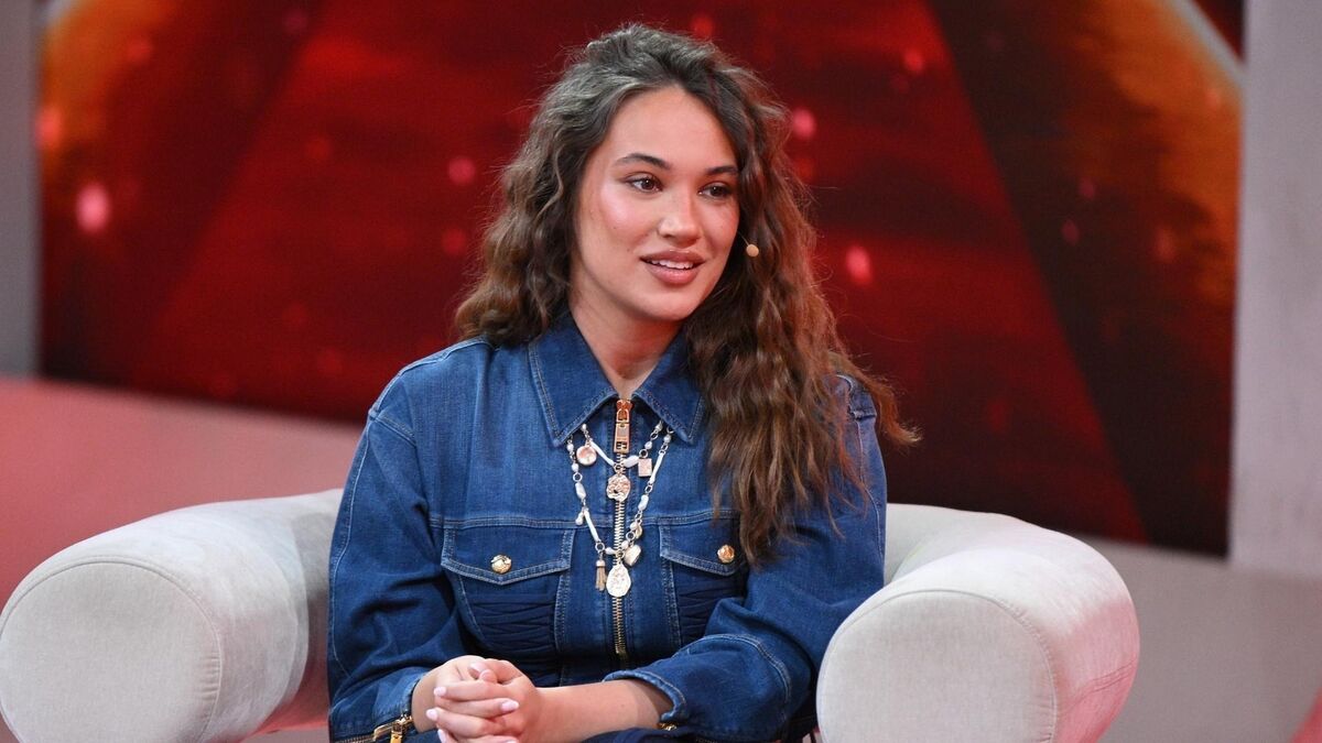 Alicja w programie „Pytanie na śniadanie” siedzi w jasnym fotelu w studiu telewizyjnym i uśmiecha się podczas rozmowy. Ma na sobie jeansową sukienkę zapinaną na suwak oraz wyrazisty, warstwowy naszyjnik, a do policzka przypięty mikrofon. W tle widać czerwone, rozświetlone elementy scenografii charakterystyczne dla programu śniadaniowego.