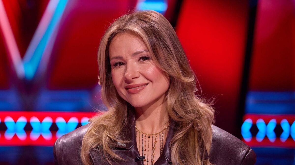 Anna Karwan ma długie, falowane włosy i jest zwrócona w stronę aparatu. Ma na sobie ciemną skórzaną marynarkę oraz ozdobny naszyjnik z wiszącymi elementami. W tle widoczne są czerwone i niebieskie elementy scenografii telewizyjnego studia.