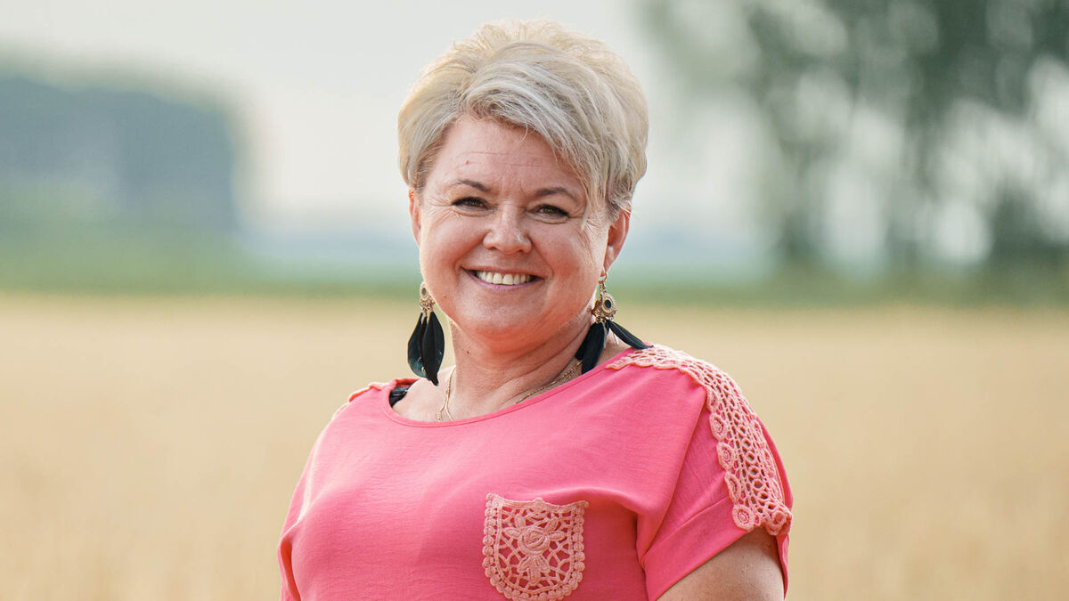 Agata z programu „Rolnik szuka żony” ma krótkie jasne włosy i koralową bluzkę z ażurowymi zdobieniami. Przy uszach widoczne są długie kolczyki z czarnymi piórami. W tle rozciąga się jasne pole oraz rozmyta zieleń drzew.